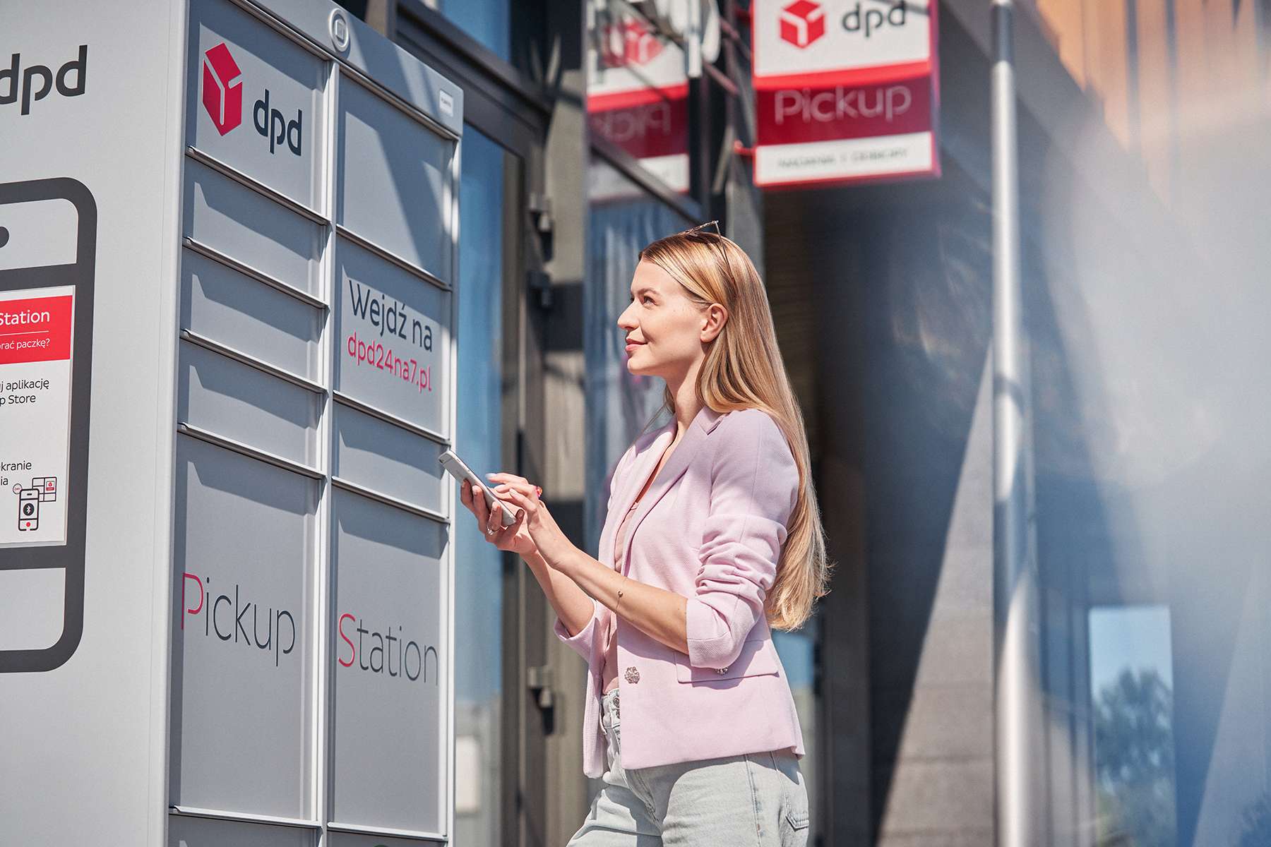 Kobieta w jasnoróżowym żakiecie używa aplikacji mobilnej DPD Polska obok automatu paczkowego